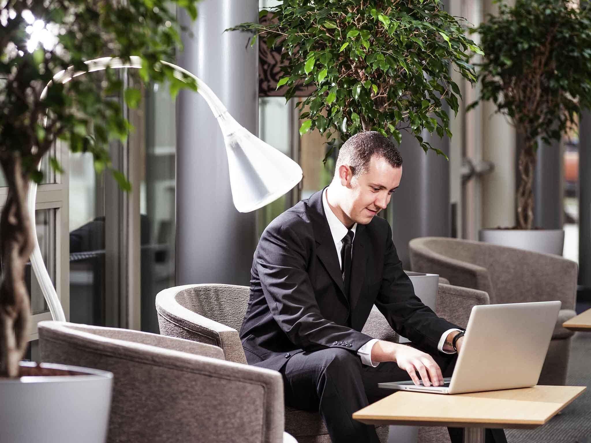 Ein Mann im Anzug arbeitet an einem Laptop in einem Innenraum mit moderner Einrichtung und Pflanzen.