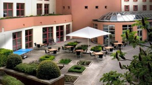Une cour dotée d’un espace extérieur aménagé, une tour horlogée et un bâtiment moderne à la façade incurvée.