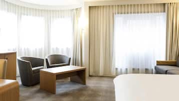 Une chambre d’hôtel avec un lit, deux fauteuils, une petite table et un bureau.