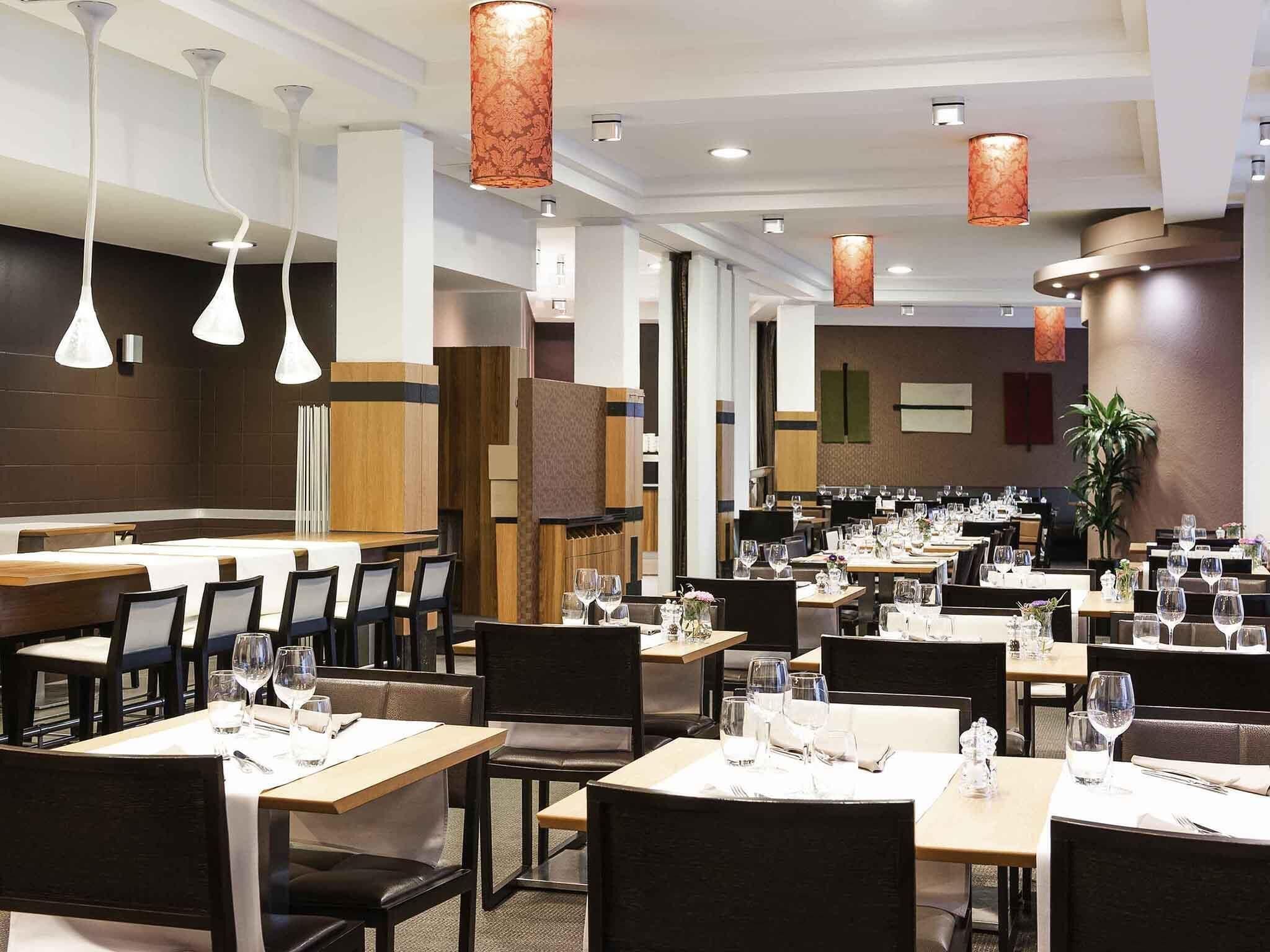A restaurant with multiple dining tables, chairs, pendant lights, and a plant.