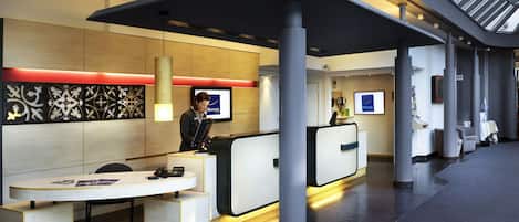 A hotel reception area with a modern design, featuring a reception desk, a seating area, and a decorative wall.