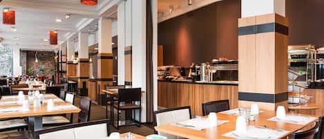 A modern restaurant with wooden tables and chairs, a kitchen area in the background, and pendant lighting.