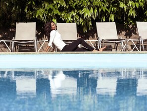 A poolside area with lounge chairs and a person lying on the edge. - Novotel Gent Centrum (Ghent)