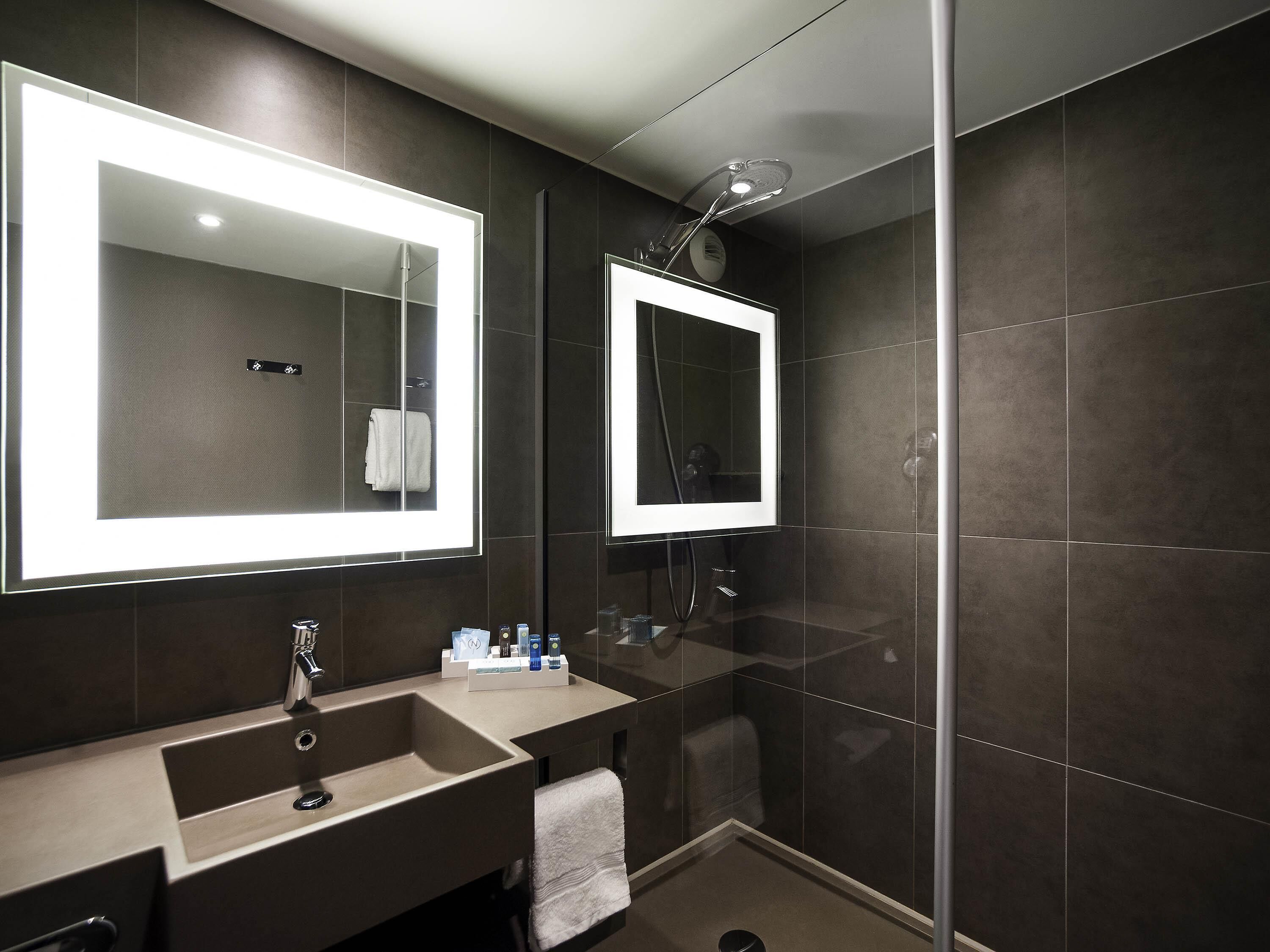 A modern bathroom with a large mirror, a sink, and a shower area.