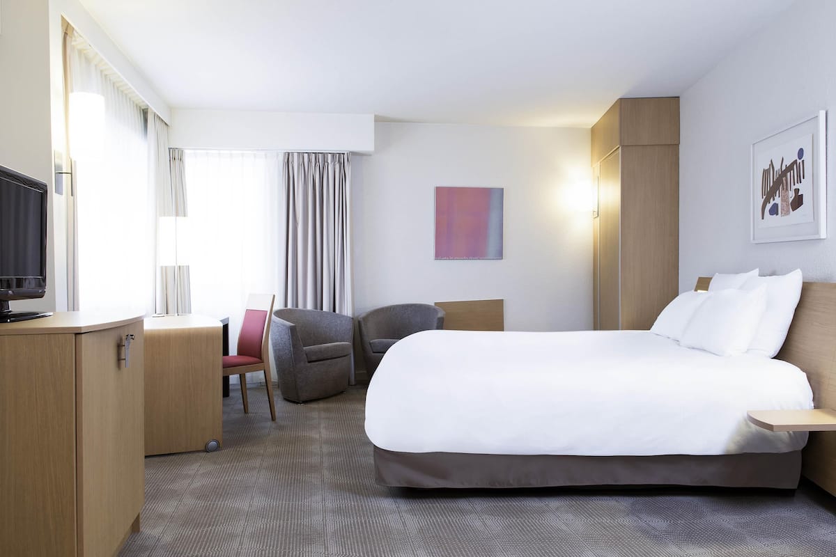 Ein Hotelzimmer mit Bett, Schreibtisch, Fernseher, Stuhl und einem Fenster mit Vorhängen.