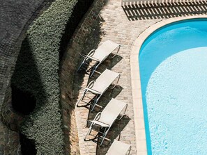 Una piscina con sillones de descanso y un muro de ladrillo.