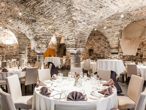 A restaurant with stone walls and vaulted ceilings, round tables set for dining. - Novotel Gent Centrum (Ghent)