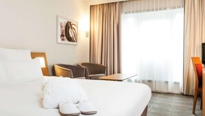 Une chambre d’hôtel avec un grand lit, un bureau, une chaise et une fenêtre avec des rideaux.