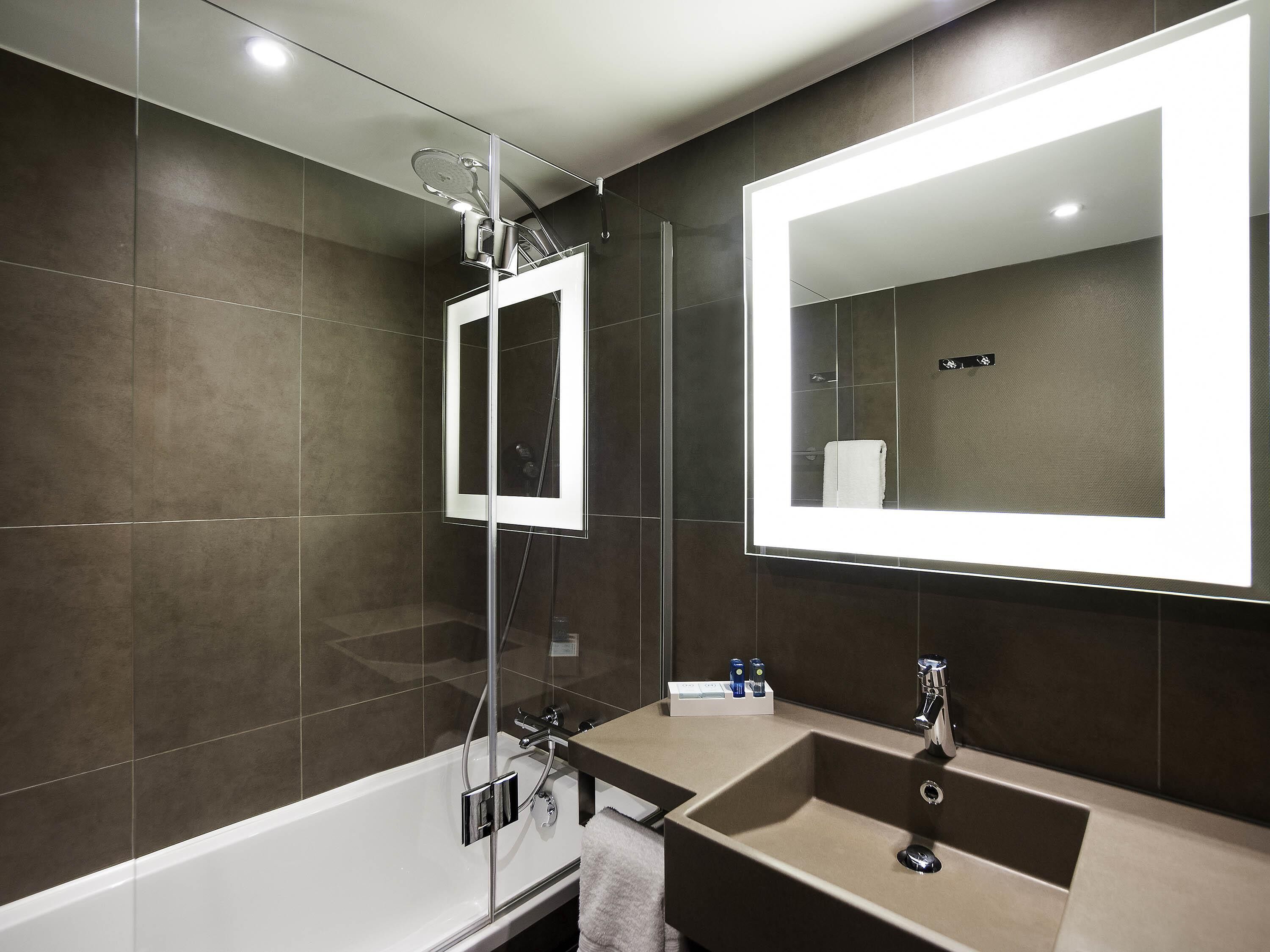 A modern bathroom with a glass-enclosed shower, a large mirror, and a beige sink.