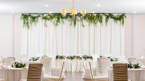 Une salle de banquet avec des tables et des chaises blanches, et un décor floral en arrière-plan.