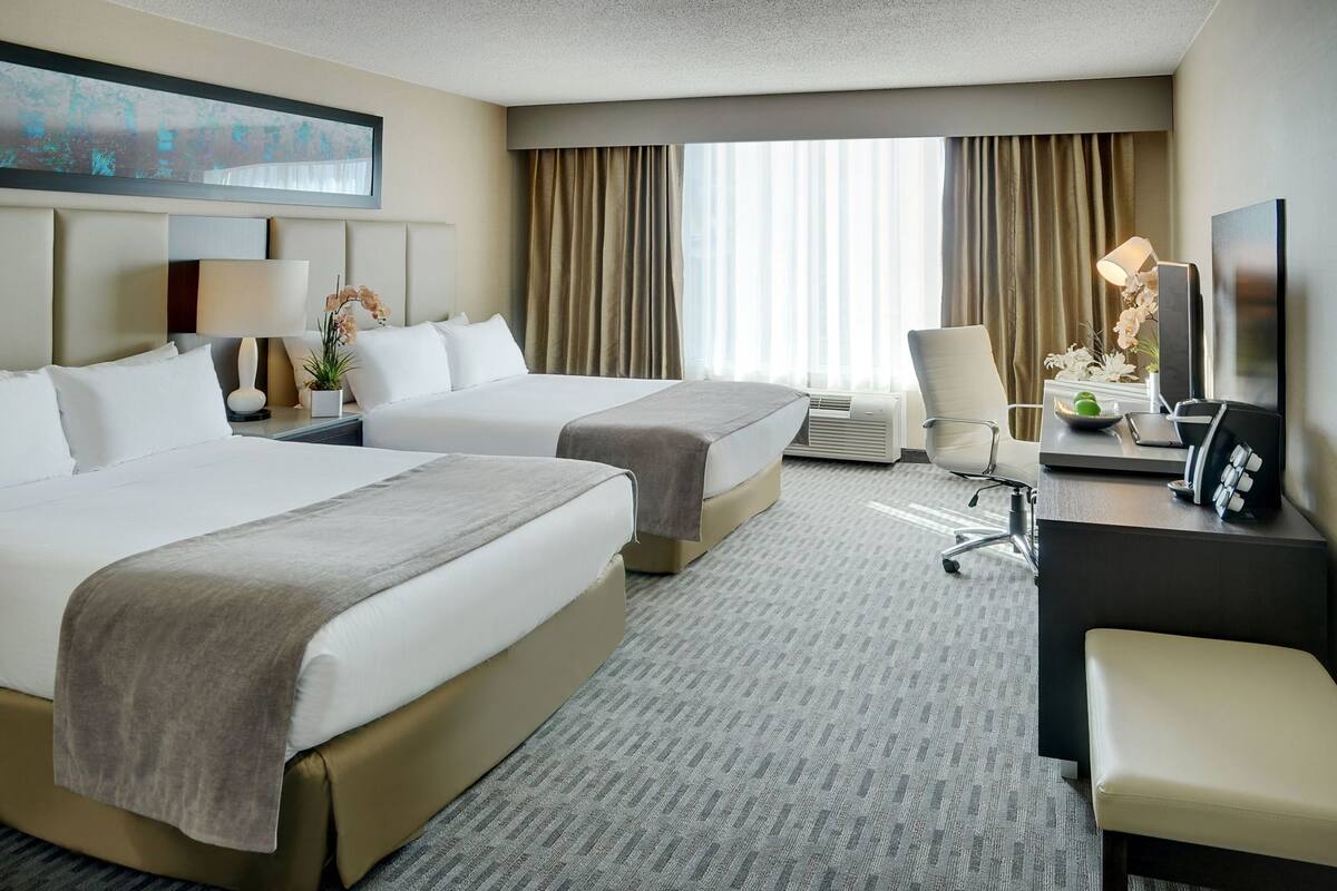 A hotel room with two beds, a desk with a lamp, a chair, and a TV.