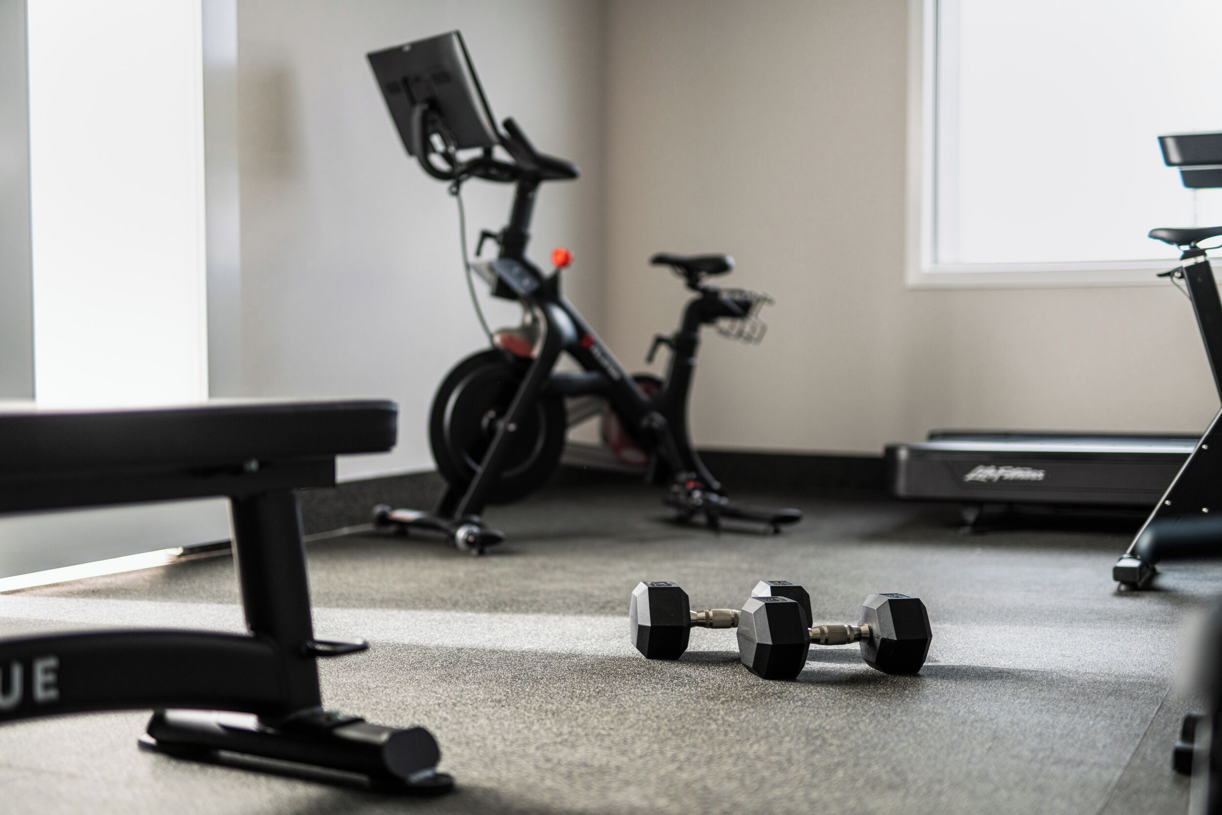 A gym with exercise equipment, a treadmill, and dumbbells on the floor.