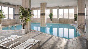 Une piscine intérieure à l’eau d’un bleu cristallin, entourée de murs et de colonnes recouverts de carreaux, et aménagée avec des chaises longues blanches.