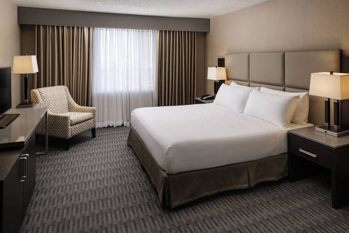A hotel room with a large bed, two bedside tables, a desk, a chair, and a TV.