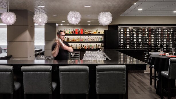 Un espace bar avec un barman, un comptoir et une étagère murale remplie de bouteilles d’alcool.