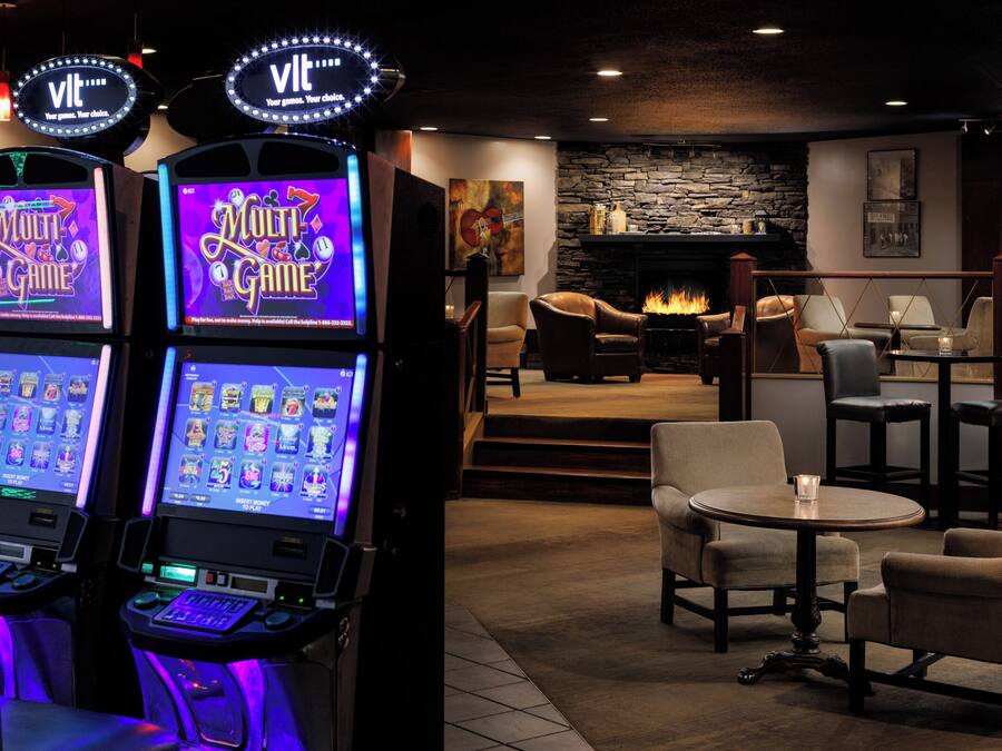 Un espace de jeux équipé de quatre bornes d’arcade proposant différents jeux, d’une cheminée en pierre, de fauteuils en cuir et d’une petite table sur laquelle est posée une bougie.