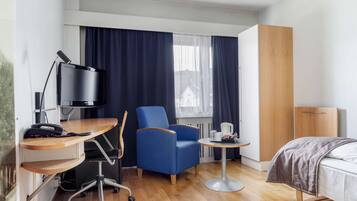 A hotel room with a desk, chair, bed, and a small table with a kettle.