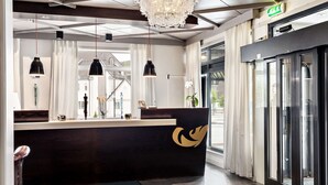 A reception area with a dark reception desk, pendant lights, a chandelier, and a glass door leading outside. - Best Western Plus Gyldenlove Hotell (Kongsberg)