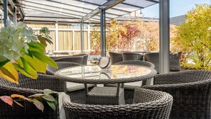 A covered outdoor seating area with wicker furniture and a glass table. - Best Western Plus Gyldenlove Hotell (Kongsberg)