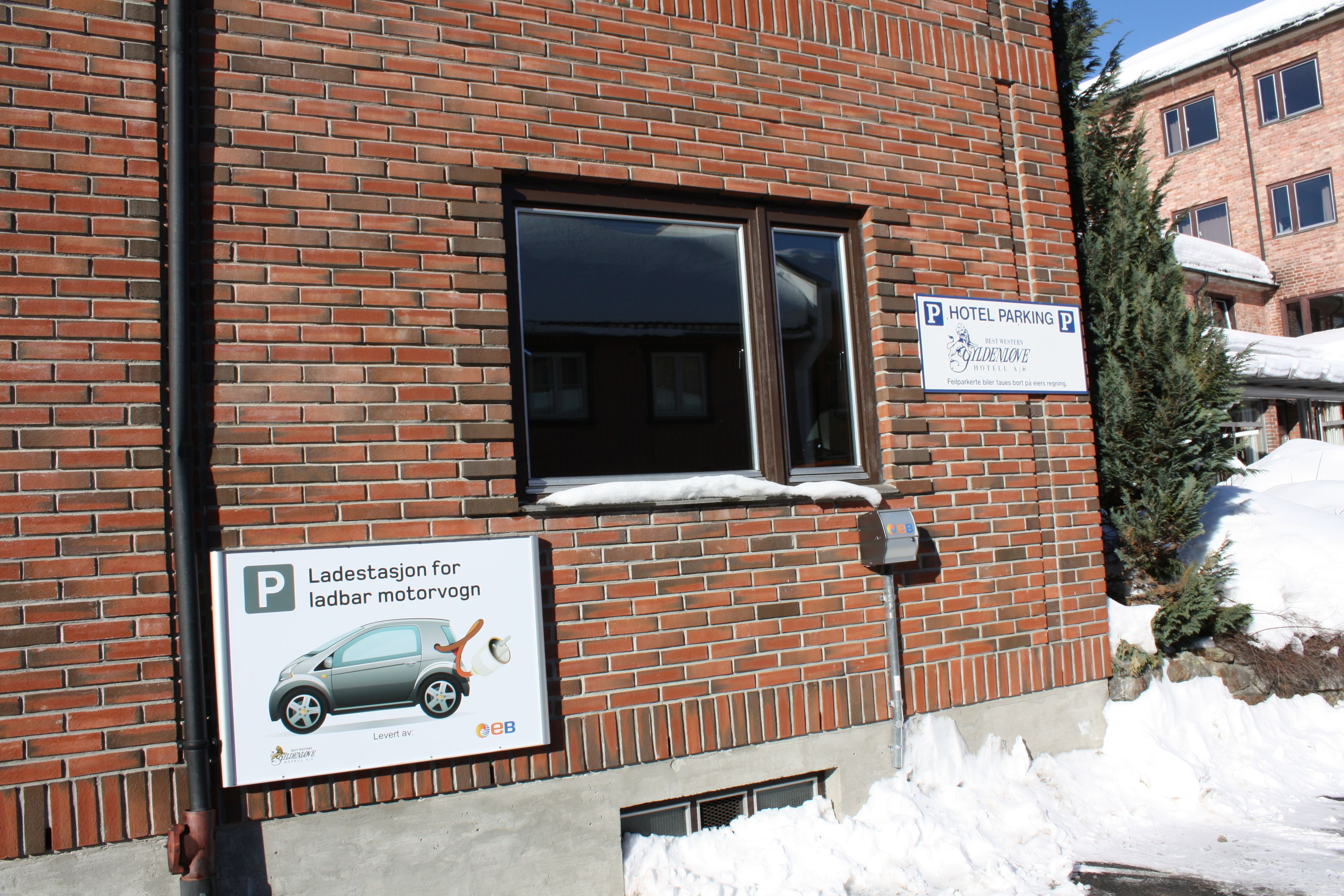A brick building with a sign indicating hotel parking and a sign for Ladestasjon for ladbar motorvogn.