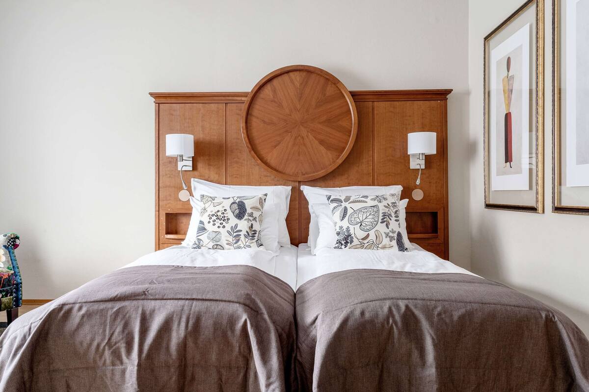 Un lit double avec une tête de lit en bois, deux lampes de chevet et des coussins à motifs floraux.