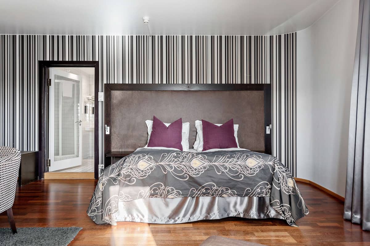 Une chambre à coucher moderne avec un grand lit, un papier peint à rayures et un plancher en bois.