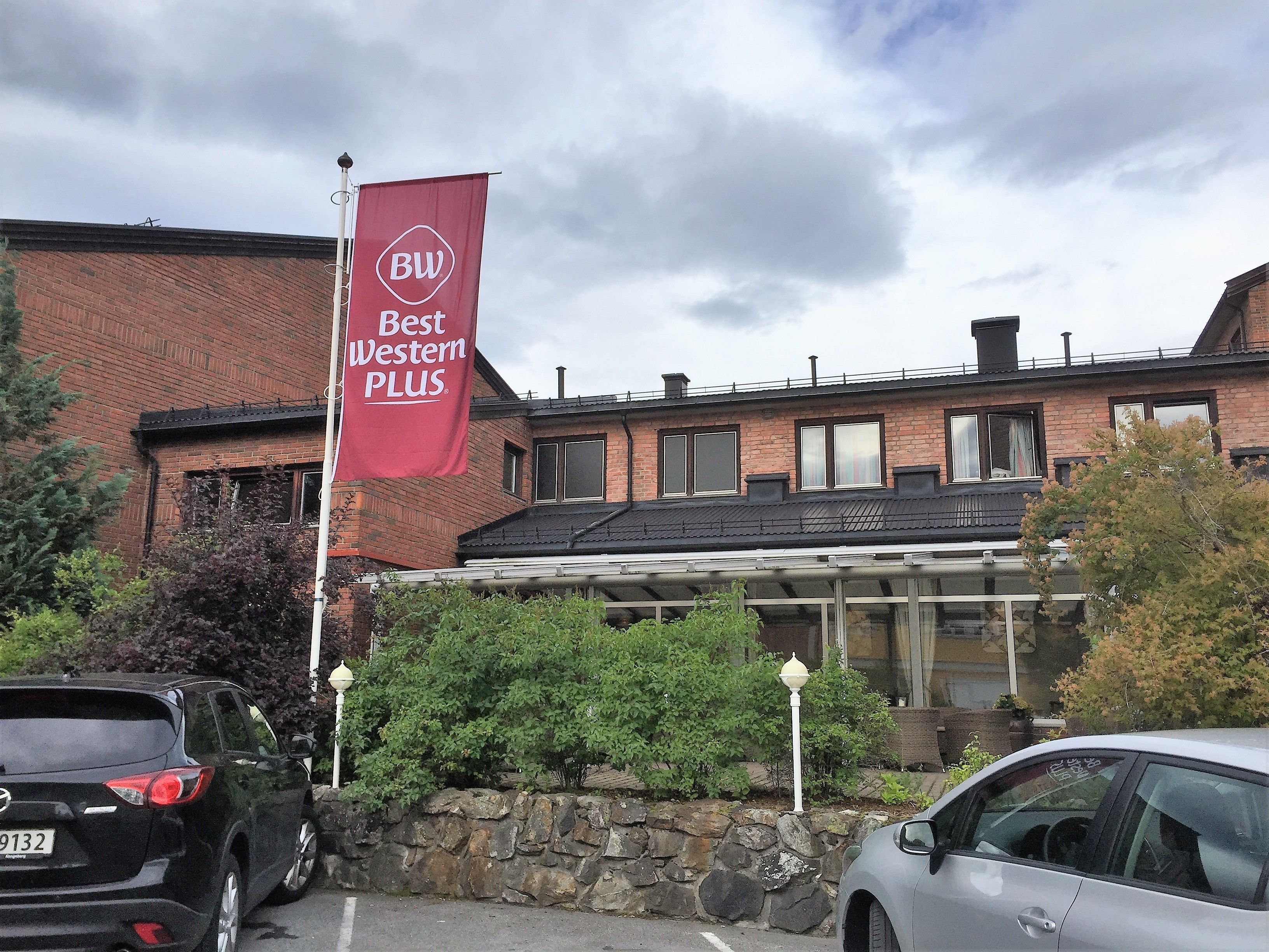 Un edificio con un cartel rojo que dice "Best Western PLUS" y un muro de piedra con vegetación al frente.