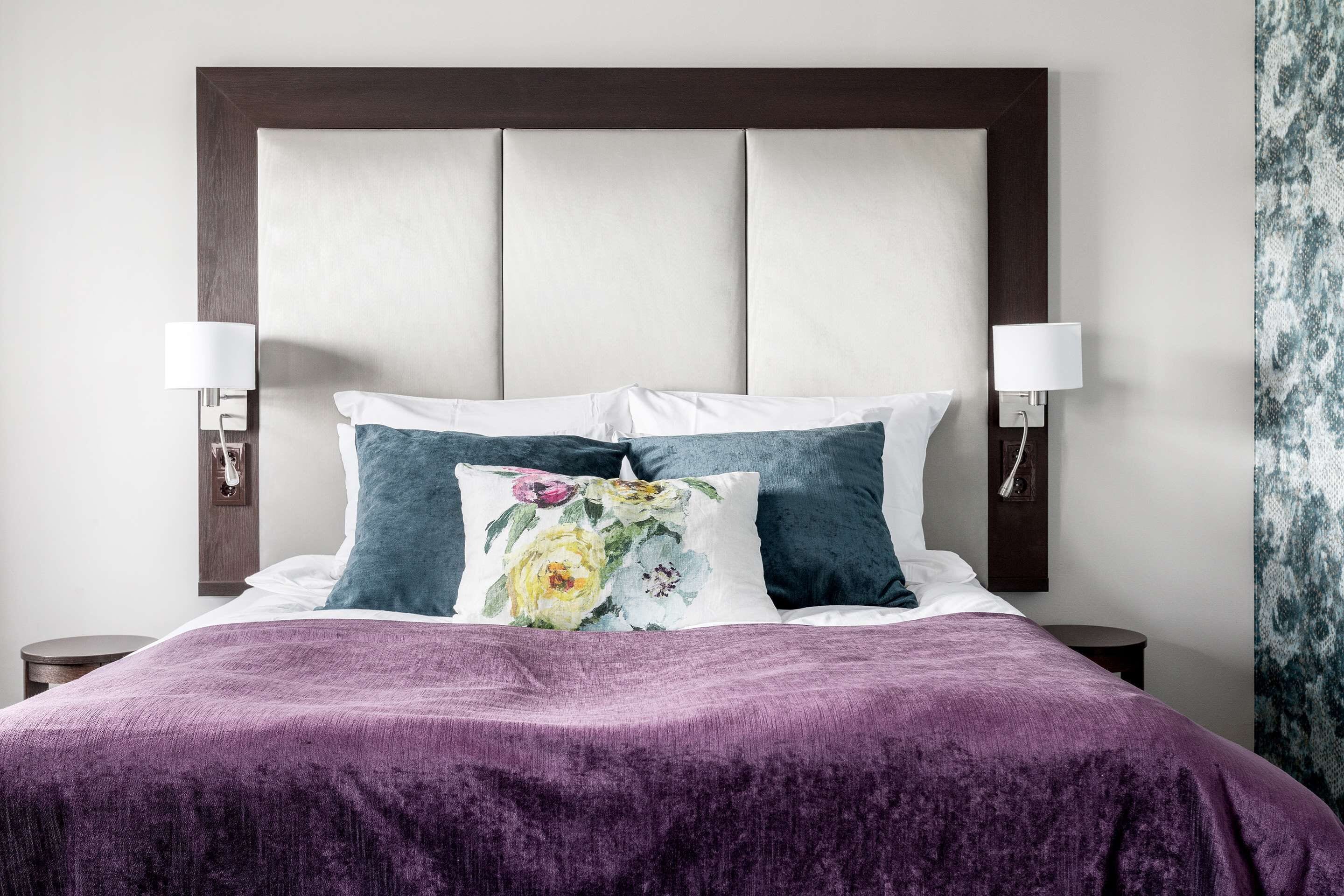 A bed with a purple bedspread, two pillows, and a headboard with a light-colored panel.