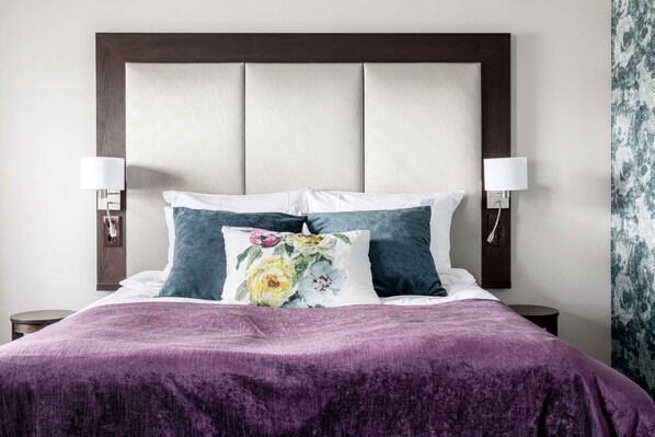 Una cama con una colcha morada, dos almohadas y un cabecero con un panel de color claro.