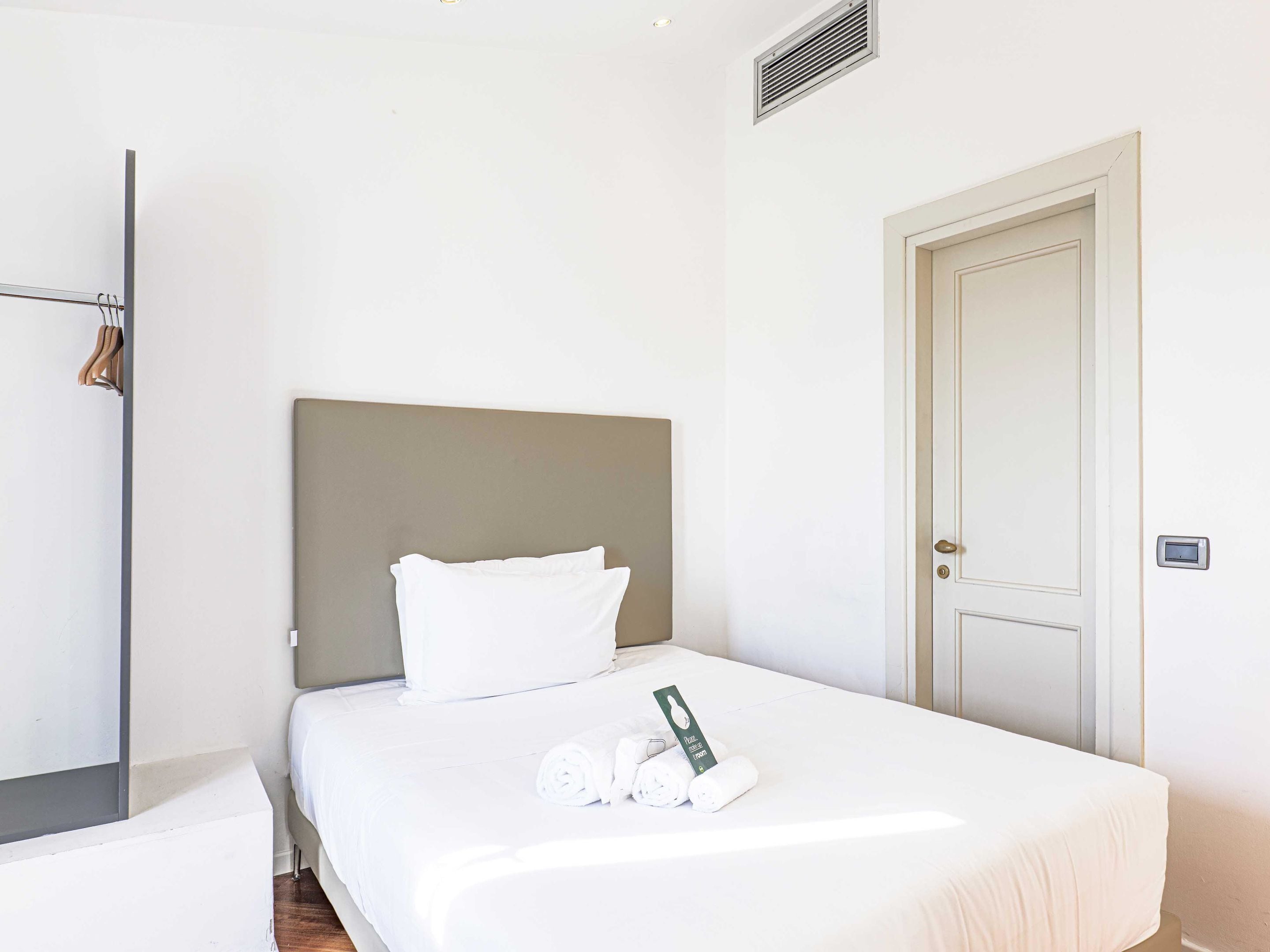A hotel room with a bed, a door, and a towel rack.