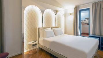 A modern hotel room with a large bed, a small round table, and a view of the city through a window.