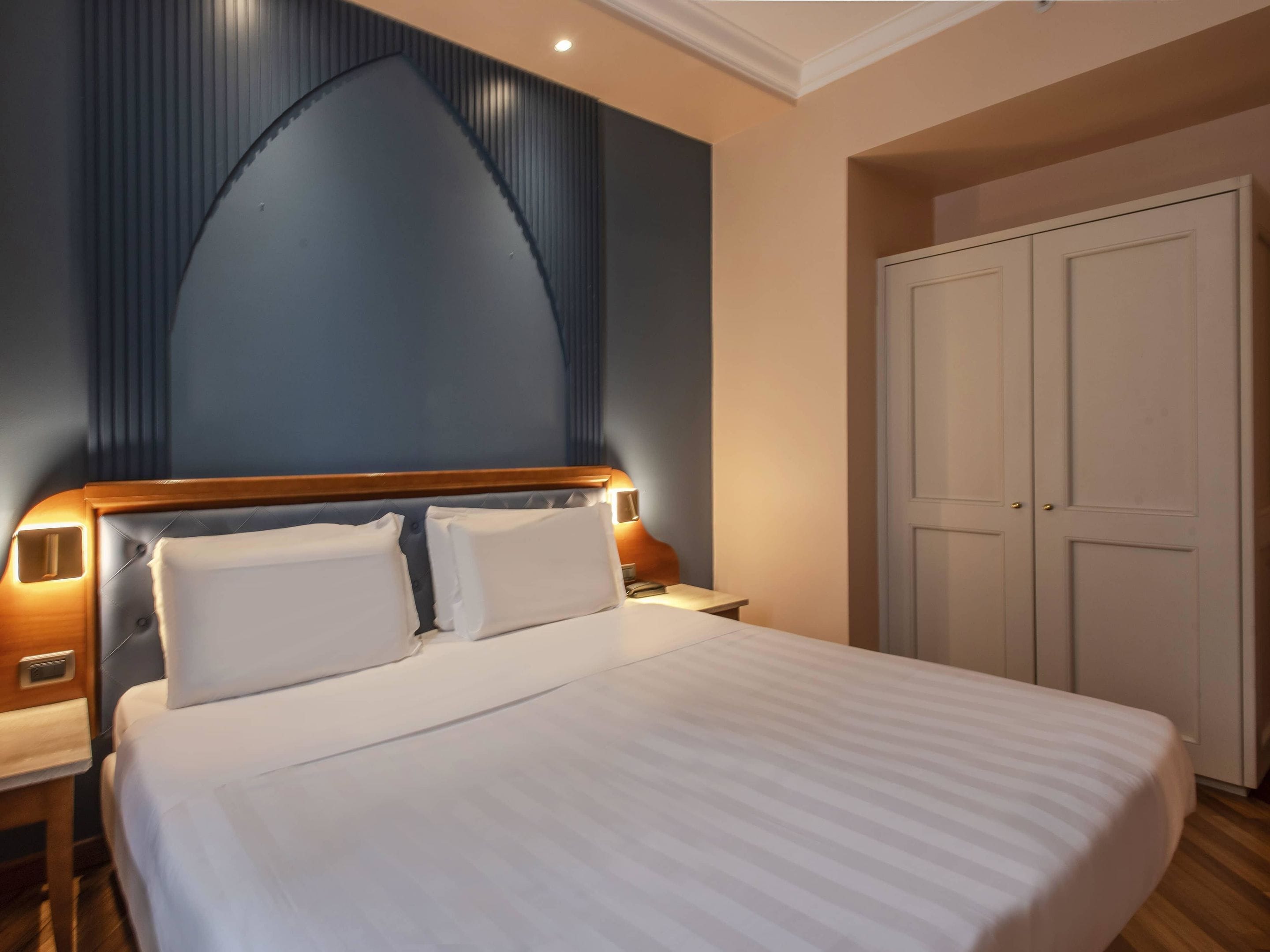 Une chambre d’hôtel avec un grand lit, une armoire et une table de chevet avec une lampe.