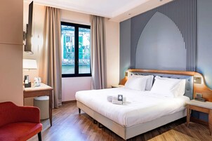 Una camera d'albergo con un letto grande, una scrivania, una sedia e vista sulla strada.