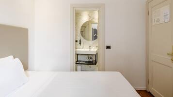 Una habitación de hotel con cama, baño con lavamanos y espejo, y puerta con un cartel.