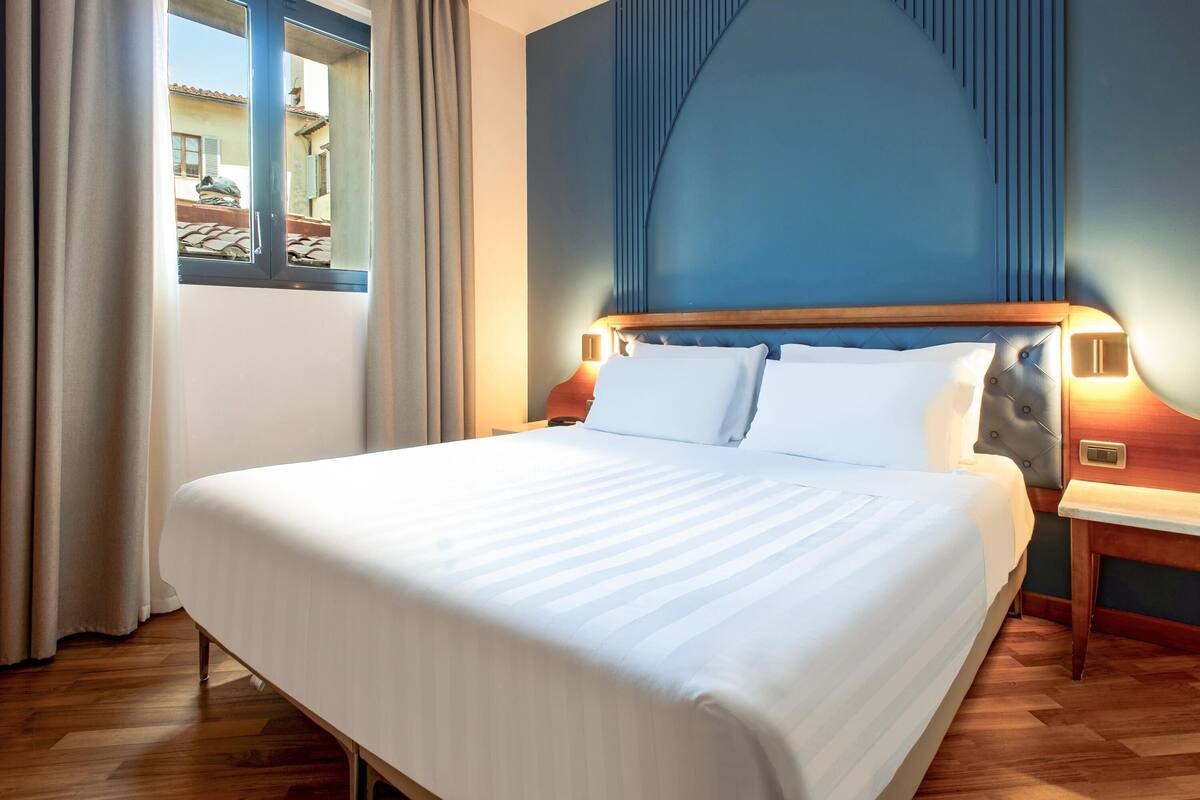A neatly made bed with white linens, a wooden headboard, and two bedside lamps.