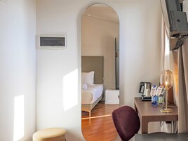 Una camera d'albergo con un letto, una scrivania con una lampada, una sedia e uno sgabello.
