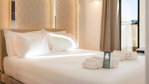 Hotellihuone, jossa on suuri sänky, pääty, ikkuna verhoilla ja pyyhkeet sängyllä.
