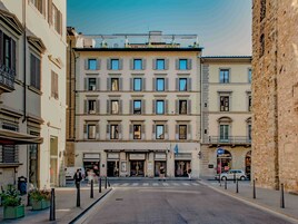 A multi-story hotel with a central entrance, balconies, and a street view.