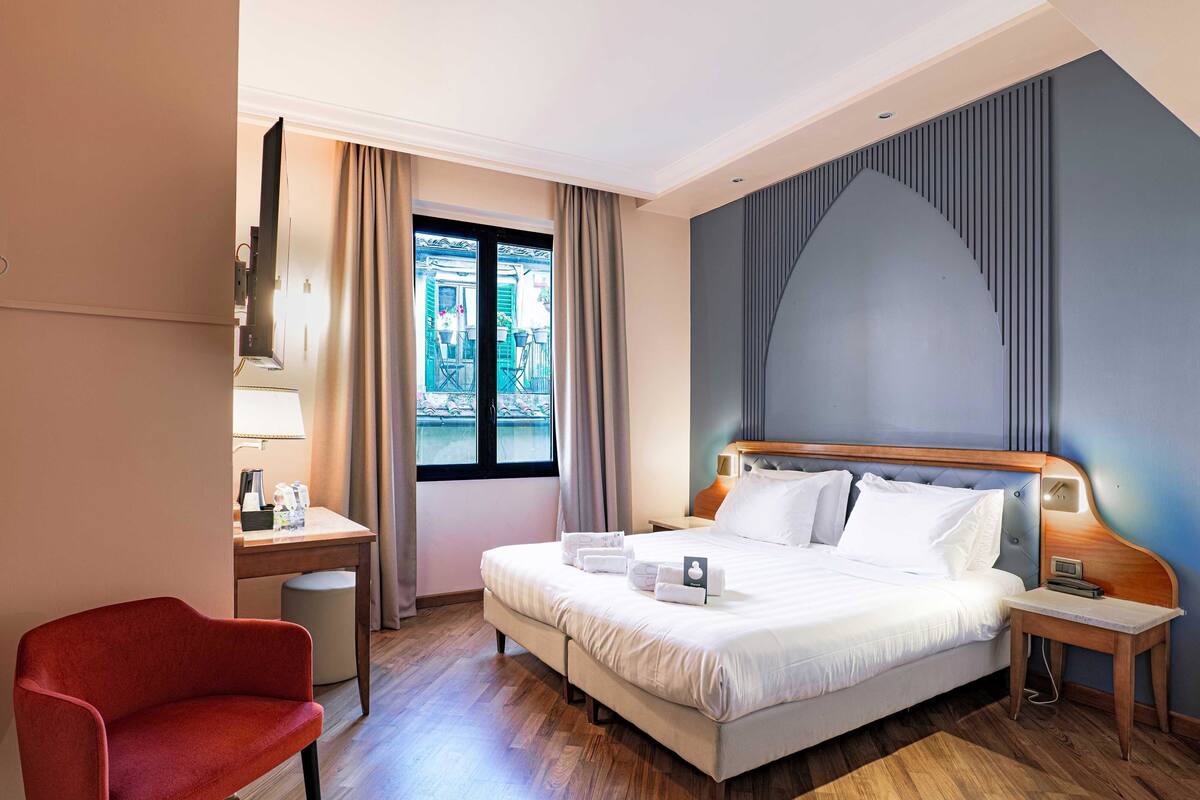 A hotel room with a bed, bedside table, lamp, chair, and a view of the outside.