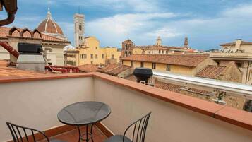 A rooftop terrace with a table and chairs, overlooking a cityscape with historic buildings and a prominent tower.