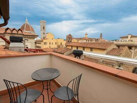 Una terrazza sul tetto con tavolo e sedie, affacciata su un panorama urbano con edifici storici e una torre imponente.
