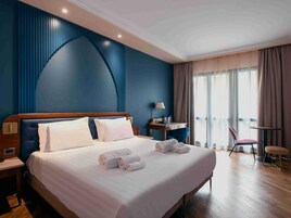 Habitación de hotel con una cama grande, un escritorio, una silla y vistas al exterior.