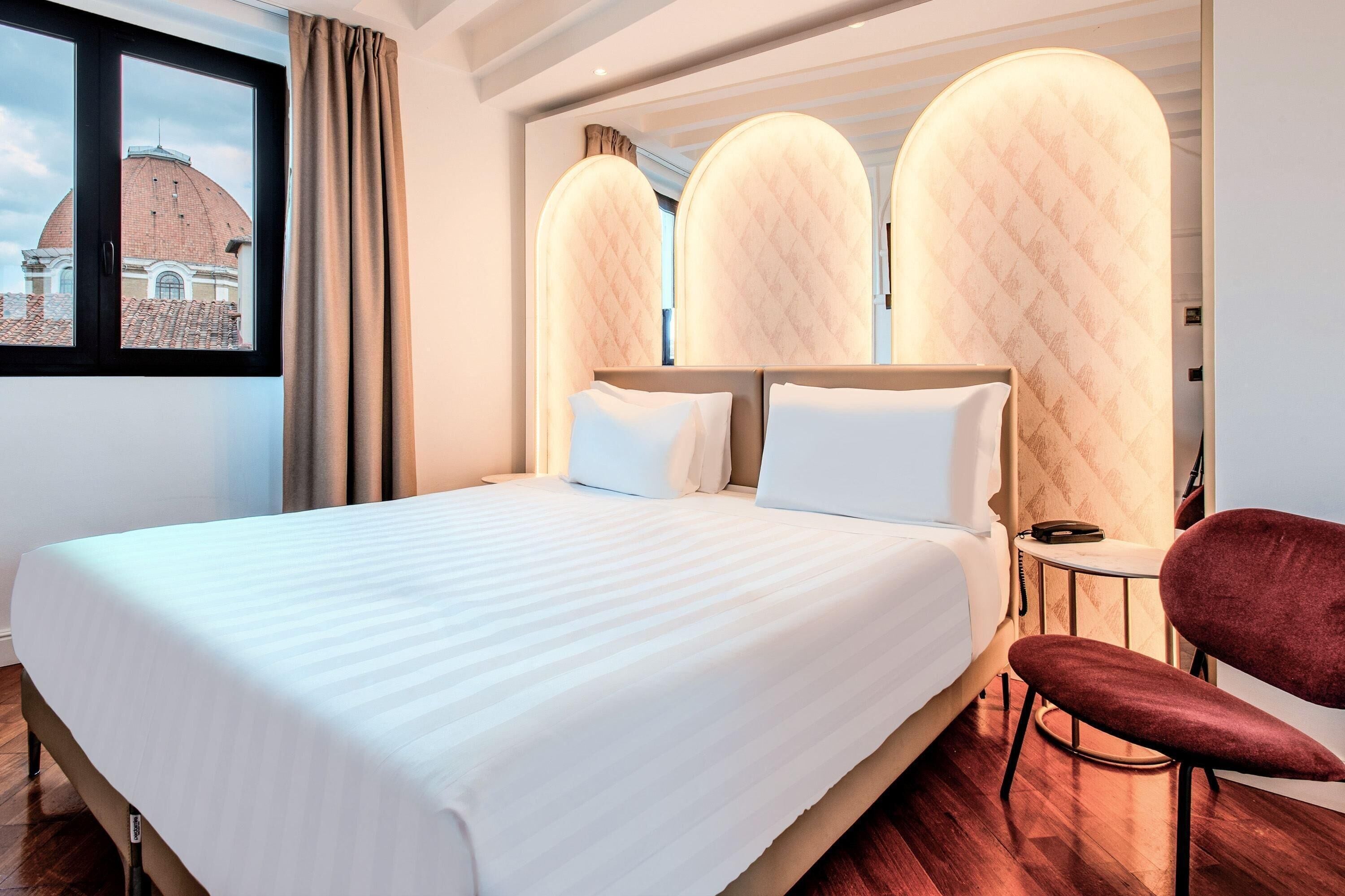 A hotel room with a large bed, a red chair, and a view of a dome building through a window.