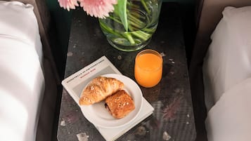 A breakfast setup with croissants on a plate, a glass of orange juice, and a book titled "Donatella P. Borgo Santonio" on a small table.