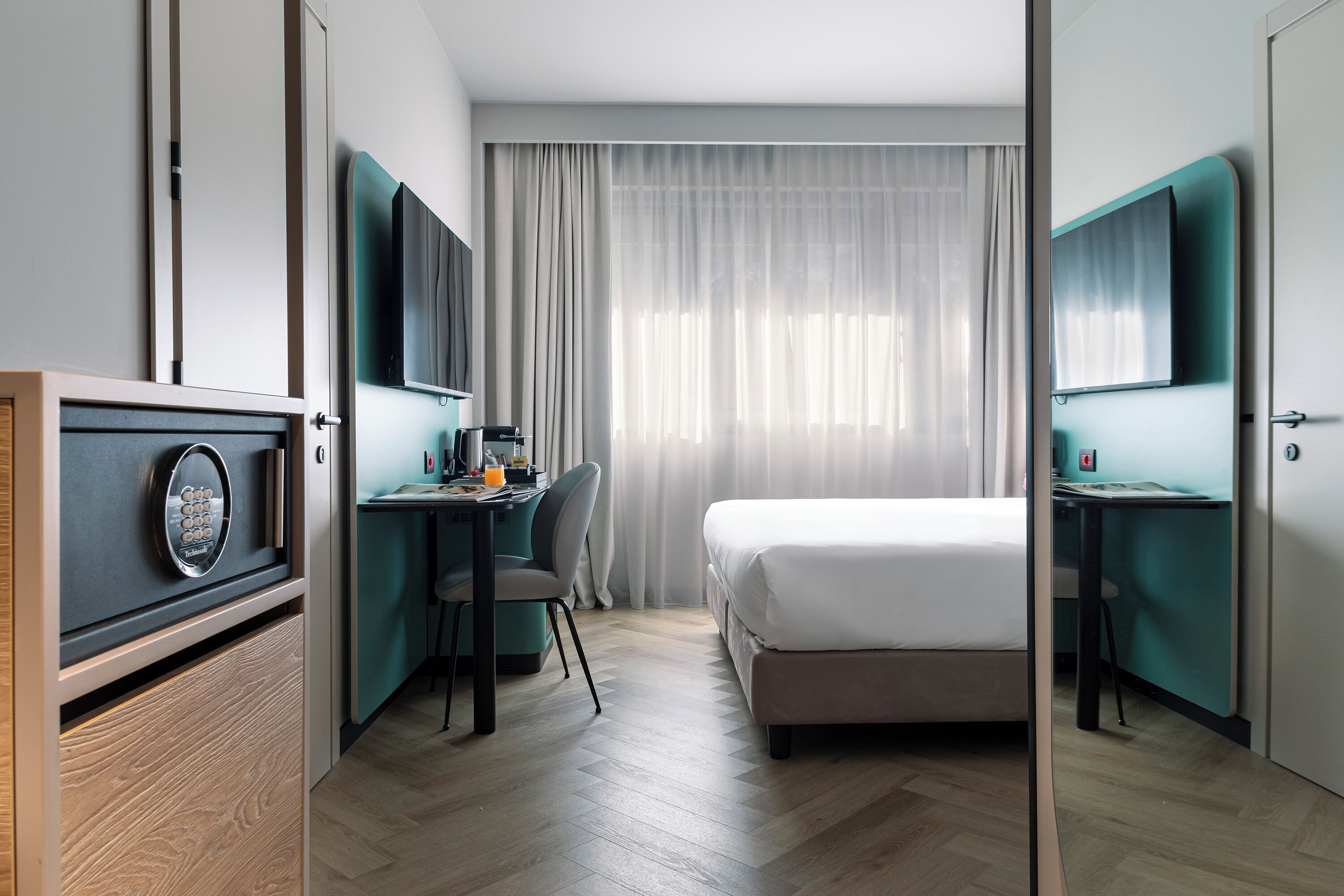 Ein Hotelzimmer mit einem Bett, einem Schreibtisch mit Stuhl, einem Fernseher und einer Minibar.
