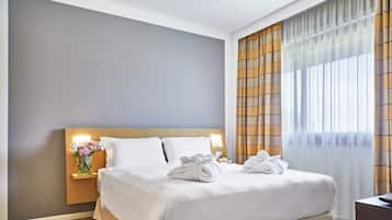 Una cama bien tendida con sábanas blancas, una mesita de noche con un florero y una lámpara en el tocador.