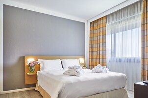 Una cama bien tendida con sábanas blancas, una mesita de noche con un florero y una lámpara en el tocador.