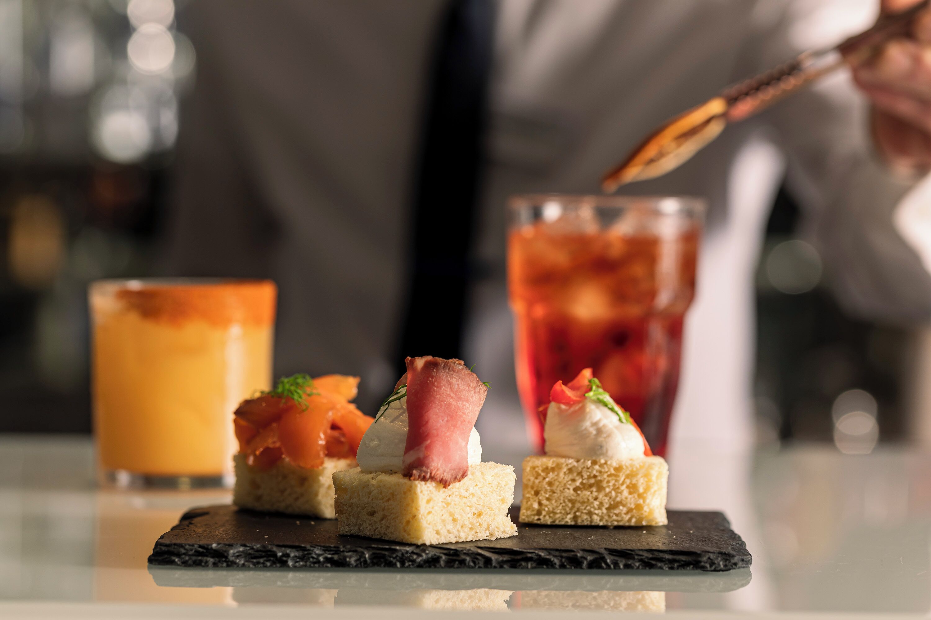 A dessert plate with three small cakes topped with various garnishes and a glass of iced tea in the background.