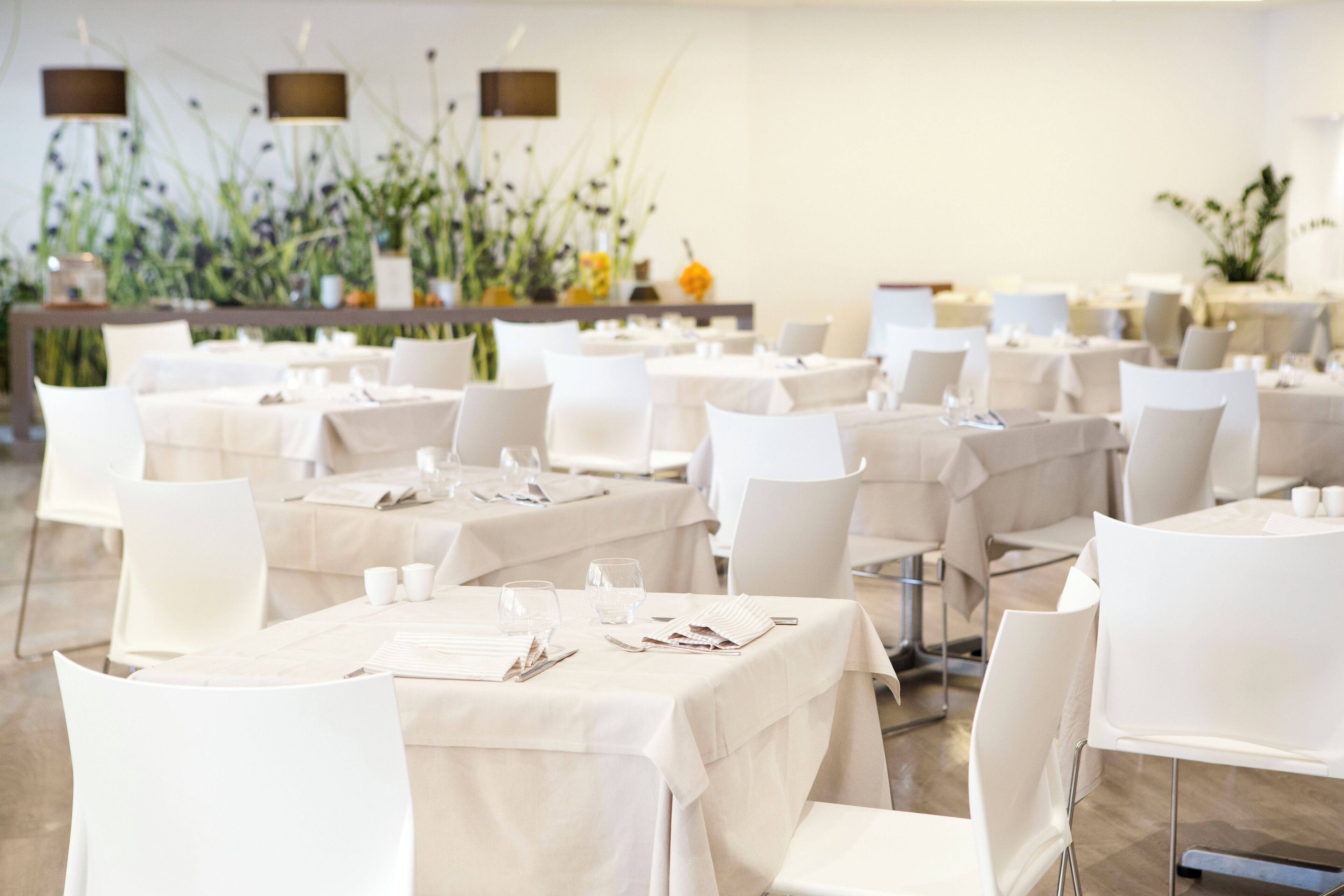 A restaurant with multiple tables set with white tablecloths and chairs, featuring a clean and modern interior.