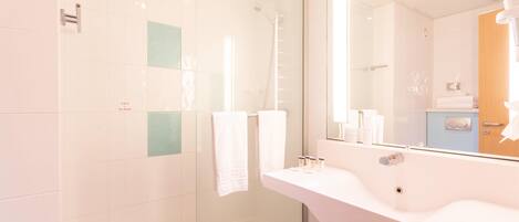 Un baño moderno con ducha envuelta en vidrio, un lavamanos blanco y un espejo grande.
